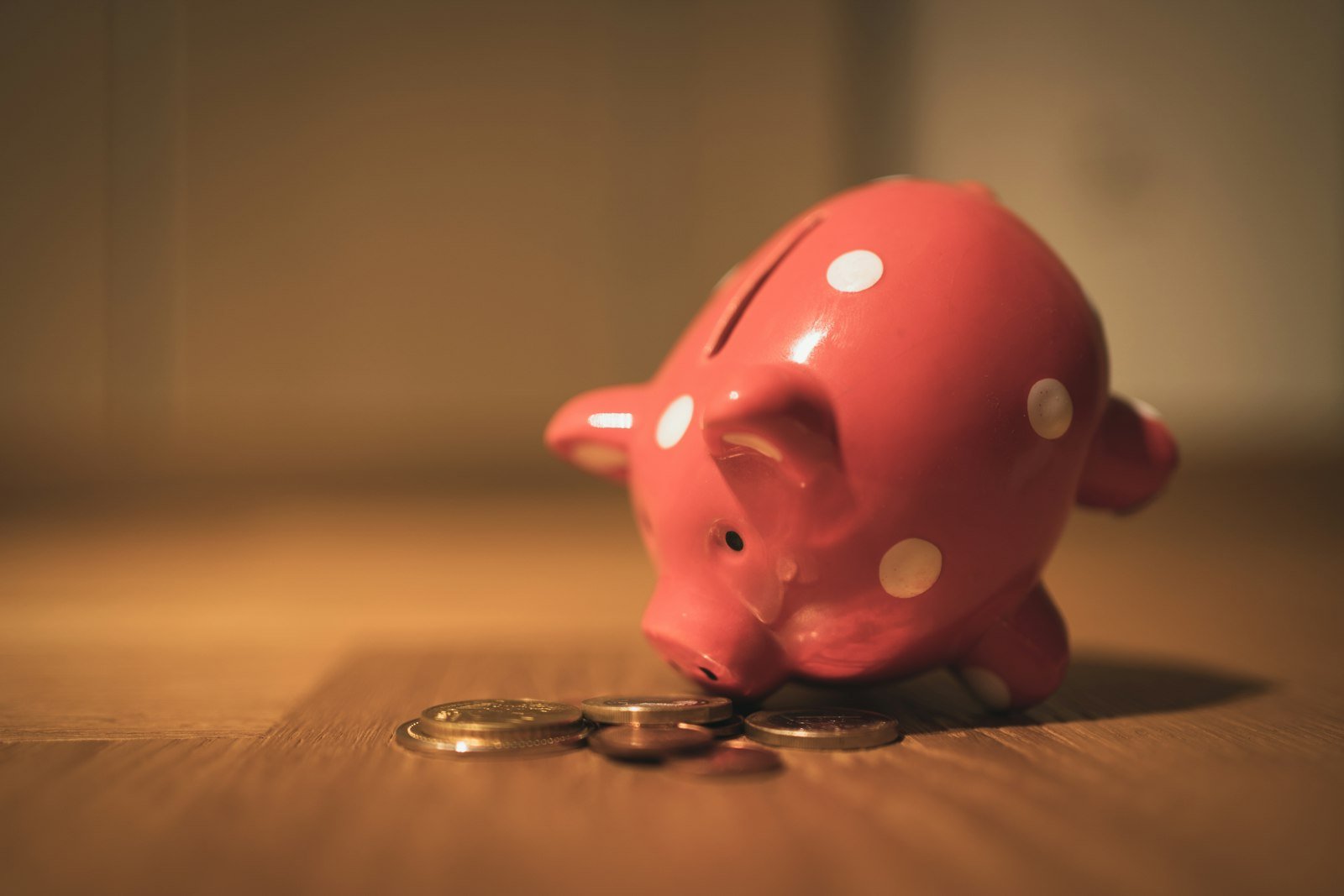 Pink piggy bank taking coins on a wooden table, symbolizing emergency savings